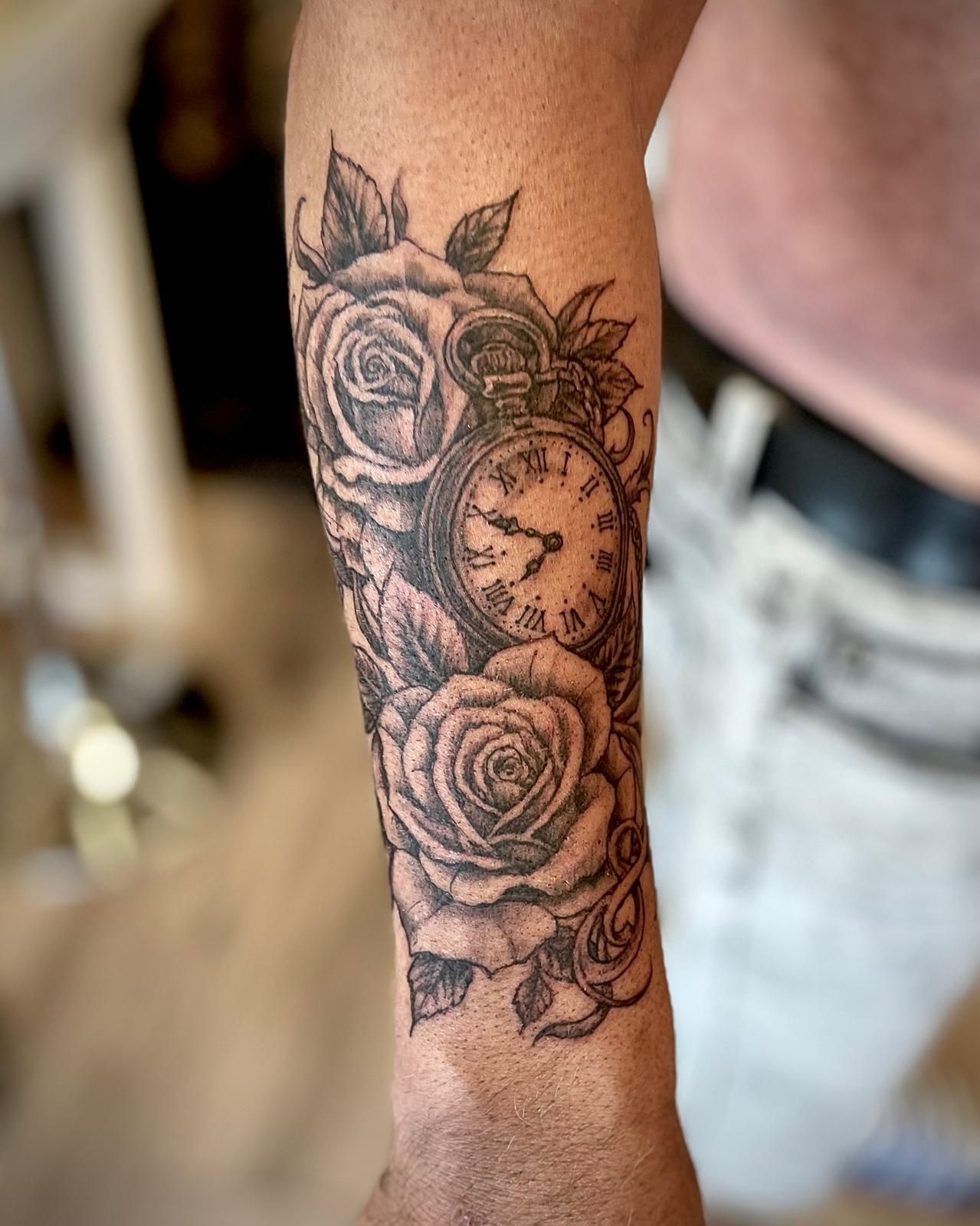 Zwart-grijze roos-tatoeage op een onderarm, met een zakhorloge in het midden.