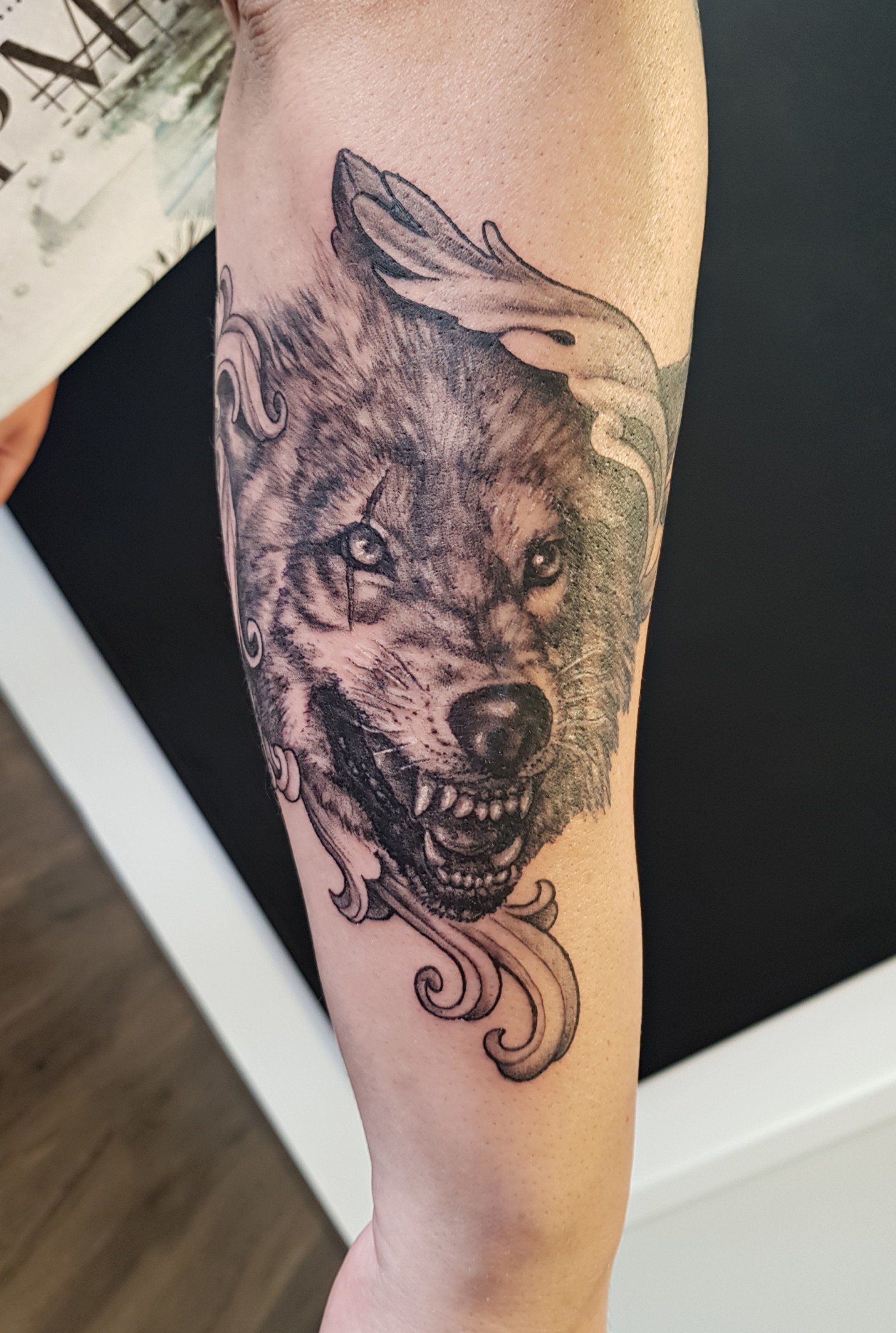Close-up van een been met een zwart-grijze wolfstatoeage op de kuit.