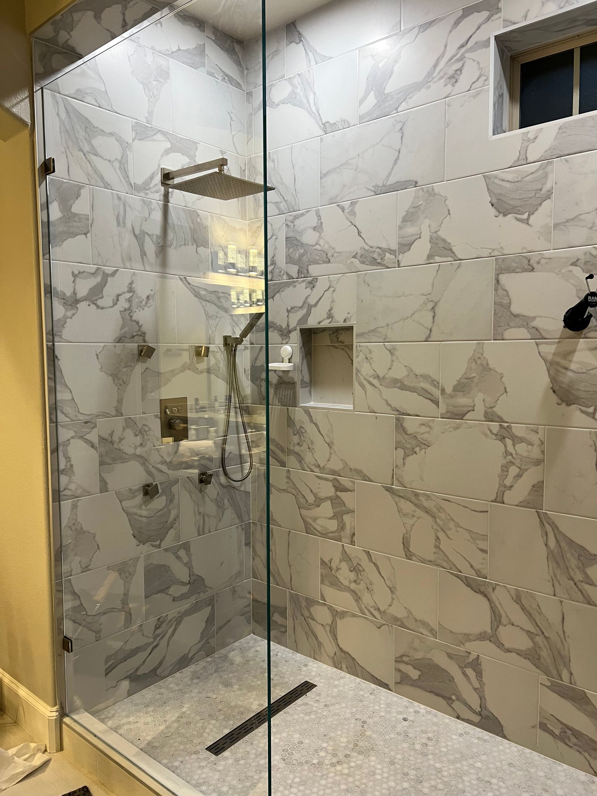 Modern tiled shower with glass enclosure, rain showerhead, and light marble-look walls with a built-in niche