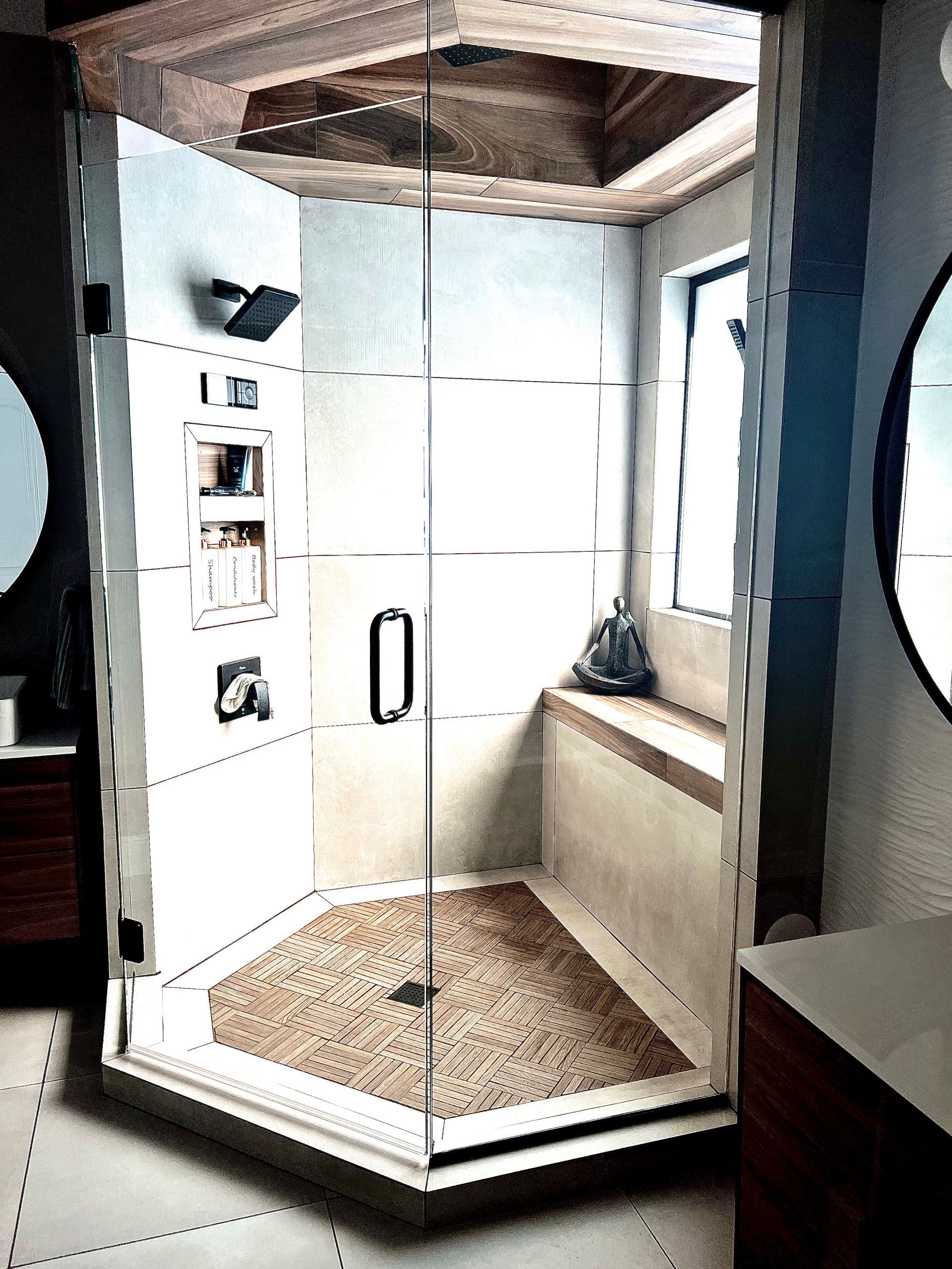 Modern octagonal shower with glass door, built-in shelves, and pebble floor in a bathroom.
