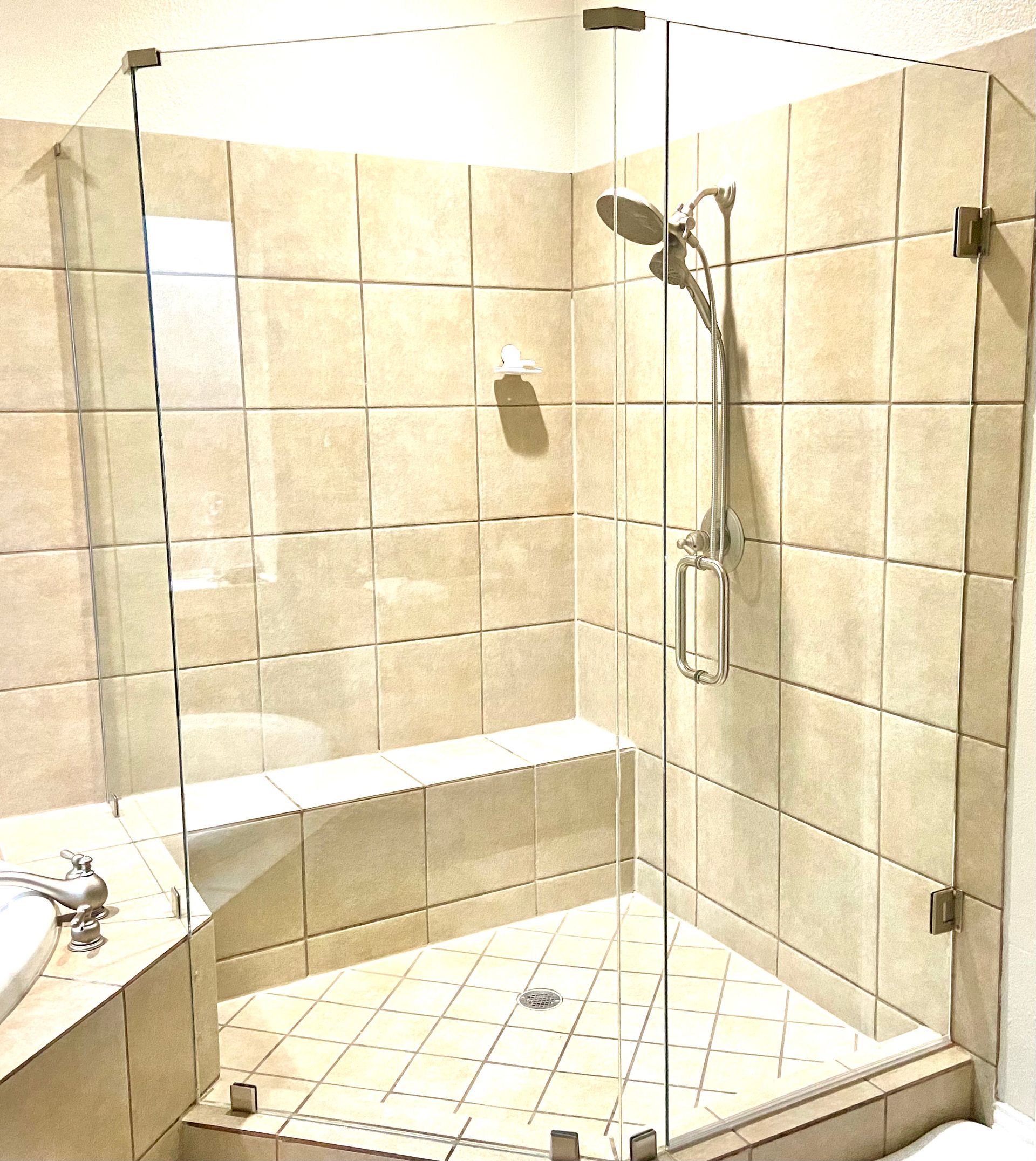 Beige tiled shower stall with built-in bench, handheld showerhead, and glass enclosure