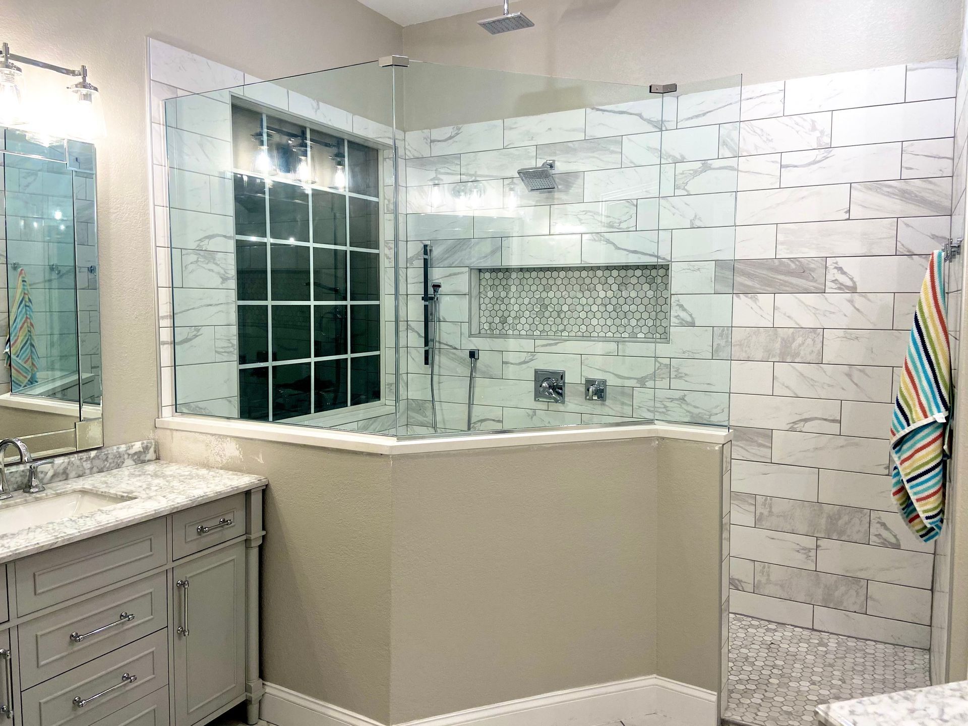 Bathroom with marble vanity, glass shower enclosure, white tile, and colorful striped towels.