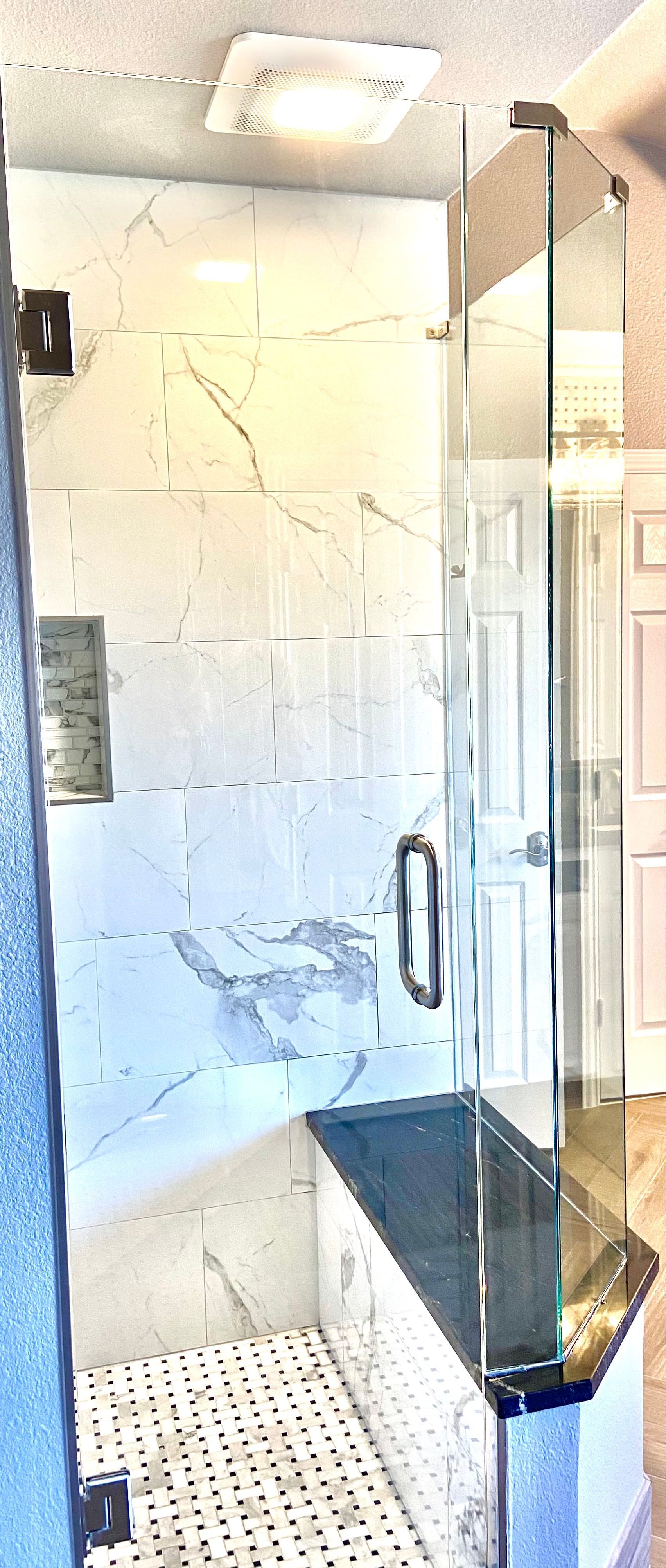 Modern bathroom shower with marble tile, glass door, and bench seat