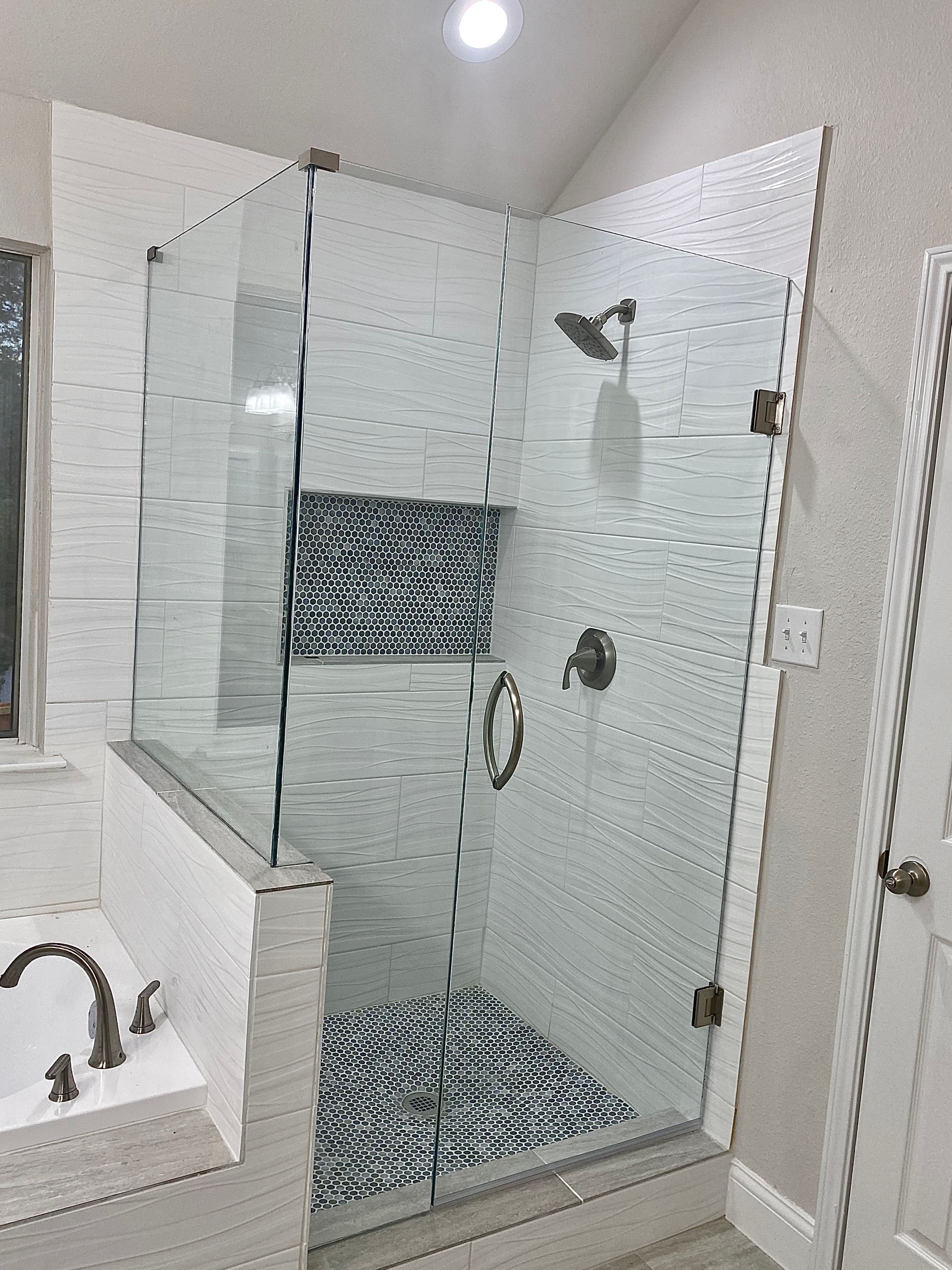 Modern bathroom with a glass shower enclosure, tiled walls, and a sink on the left.