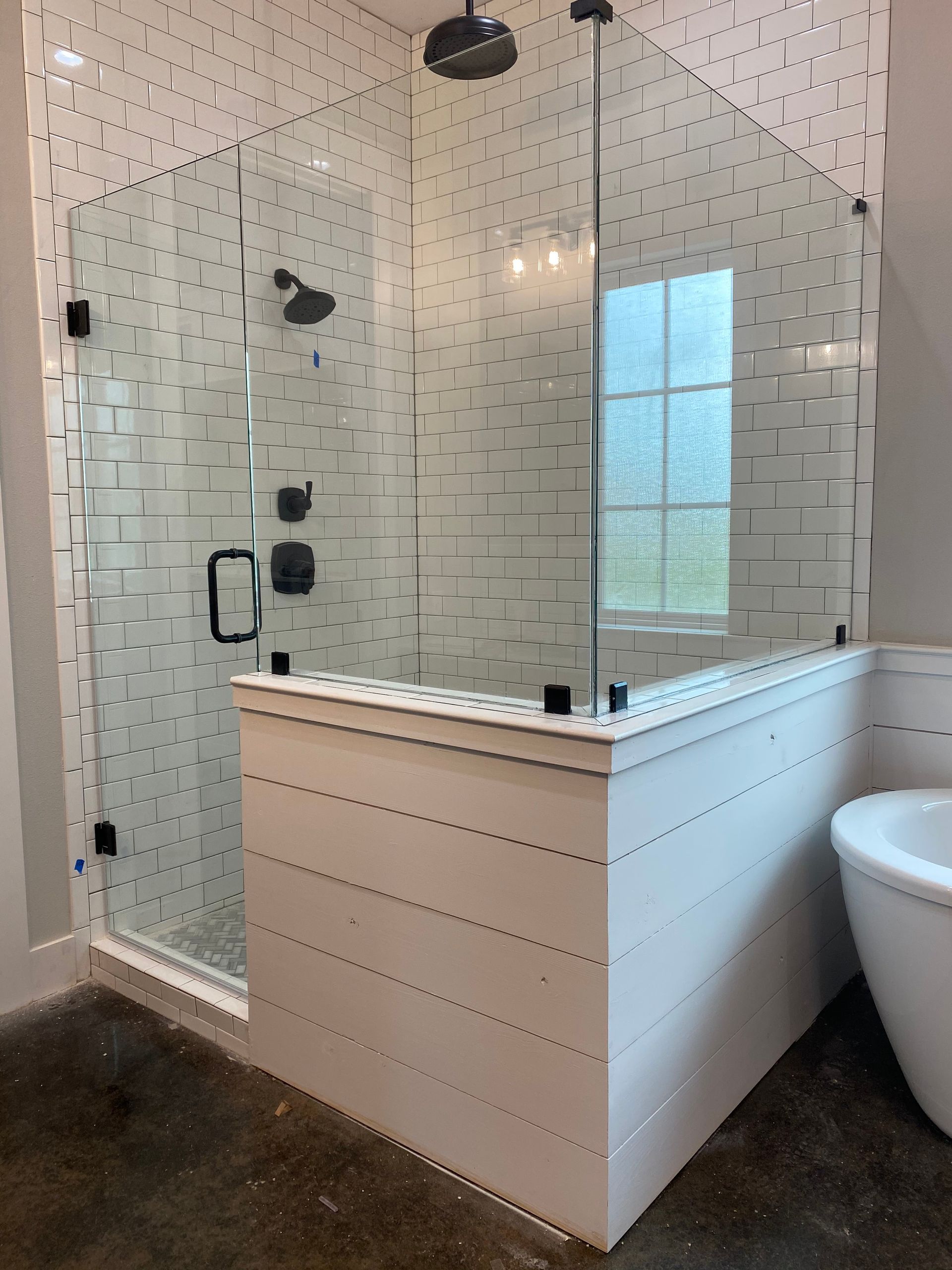 Modern bathroom with glass walk-in shower, white tile, black fixtures, and a white tub edge beside it
