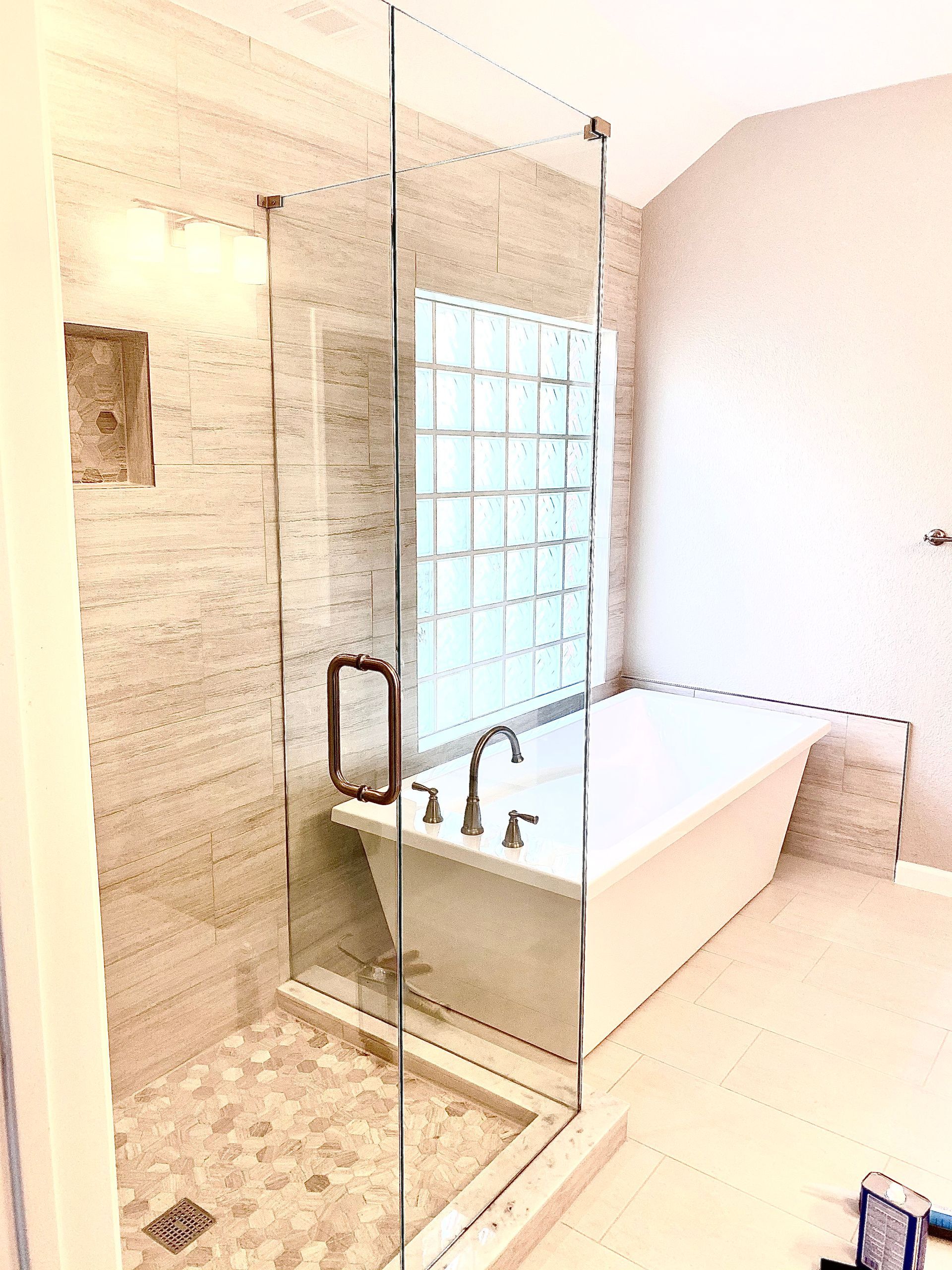 Modern bathroom with glass shower, beige stone tile, and a white freestanding tub