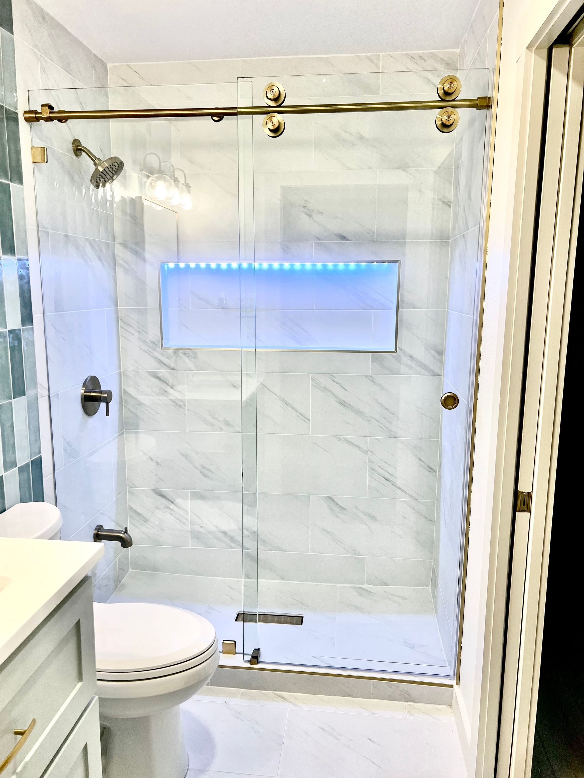 Glass shower enclosure with marble tile and blue-lit niche in a bathroom