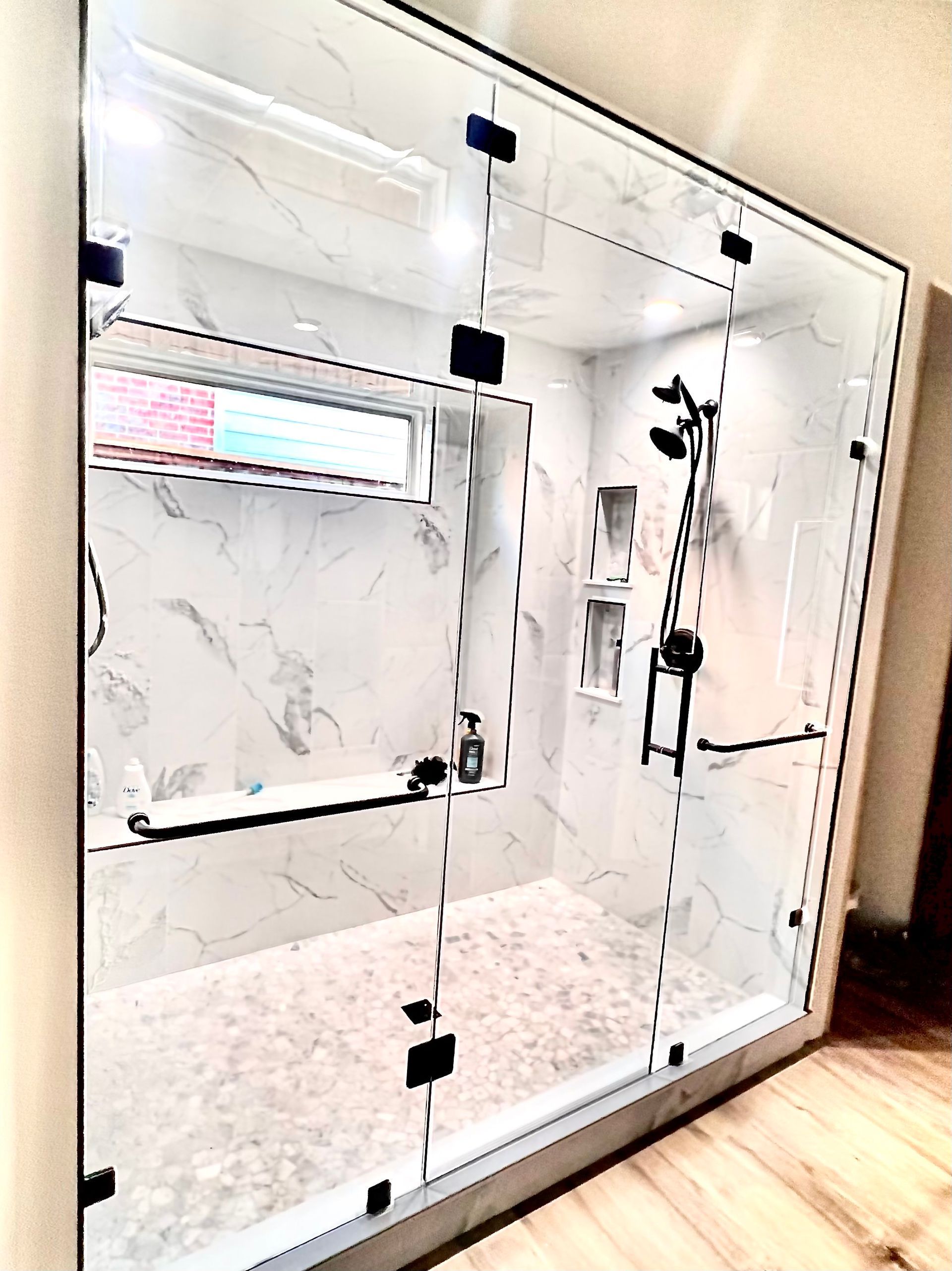 Modern glass shower enclosure with marble tile walls and chrome fixtures in a bright bathroom