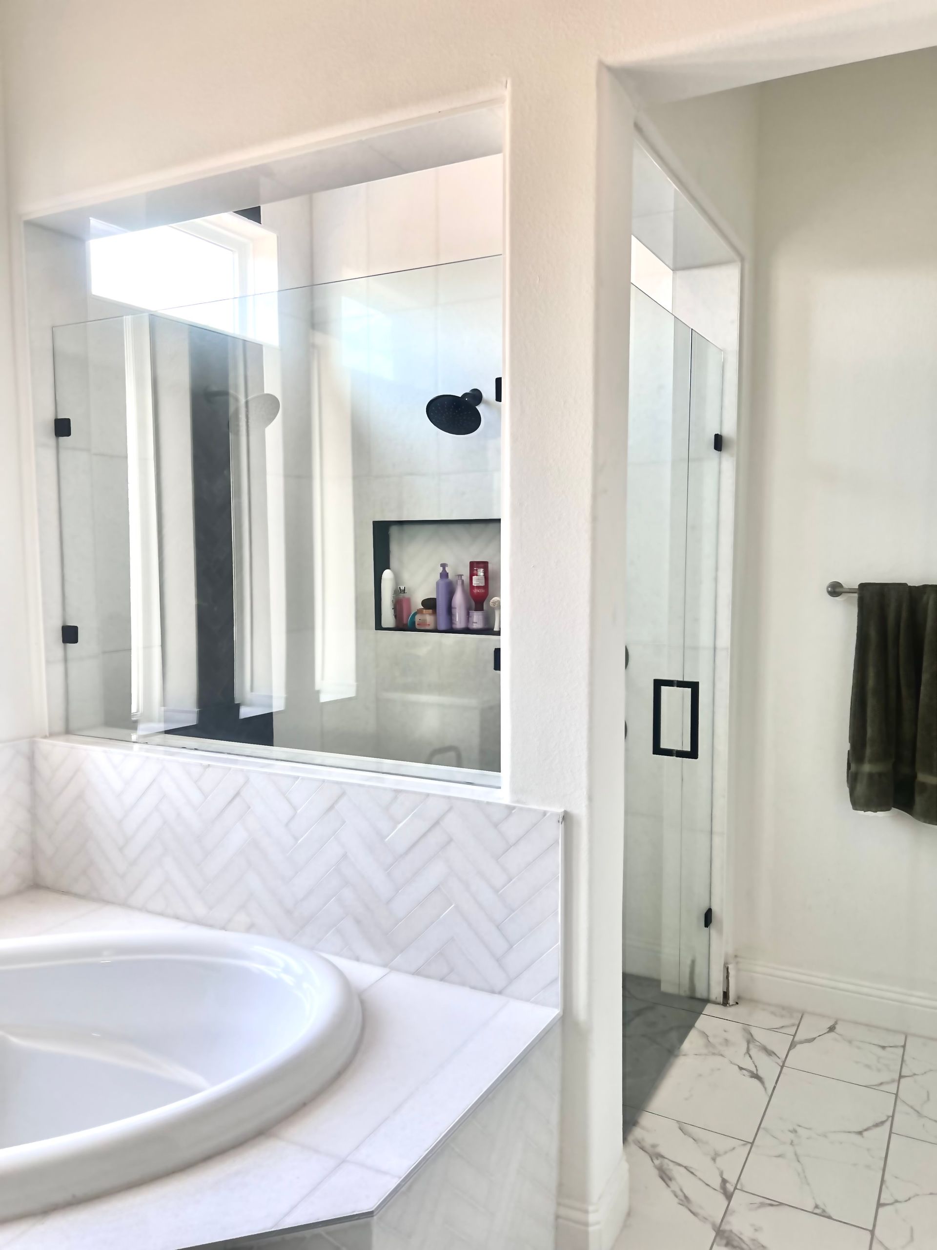 Bright white bathroom with a round soaking tub, large mirror, and towel bar by a glass shower.