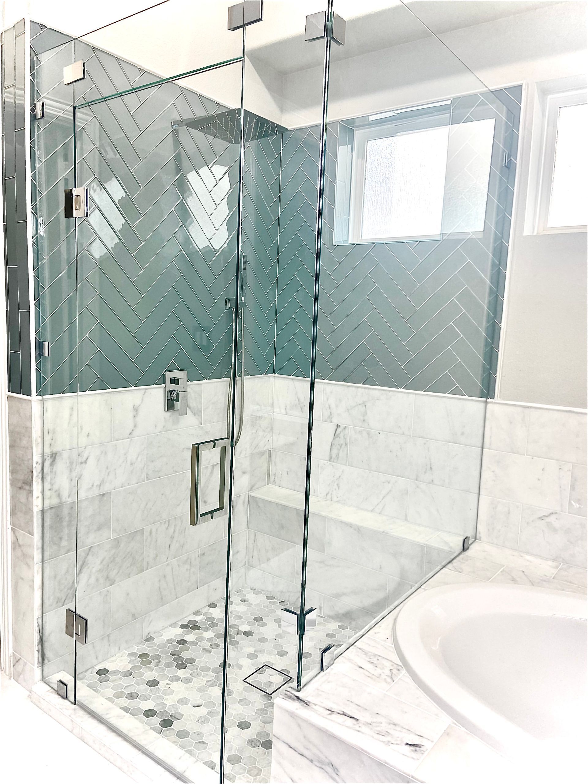 Glass shower enclosure beside a white sink in a bright tiled bathroom