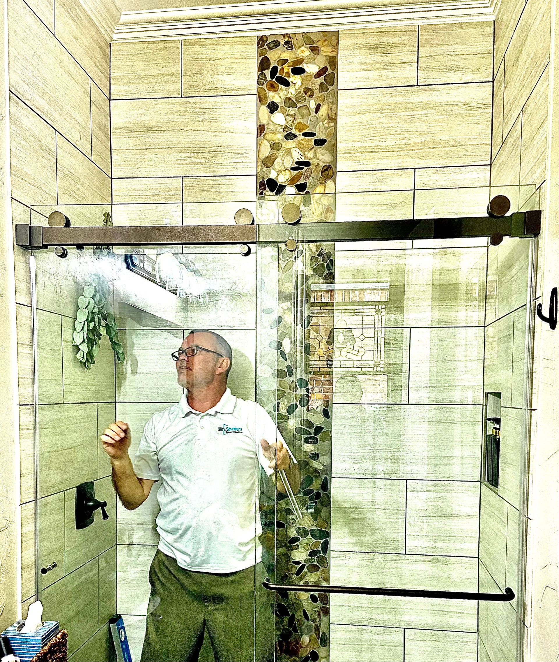Man standing inside a glass shower enclosure, looking up at the stone-tiled wall.