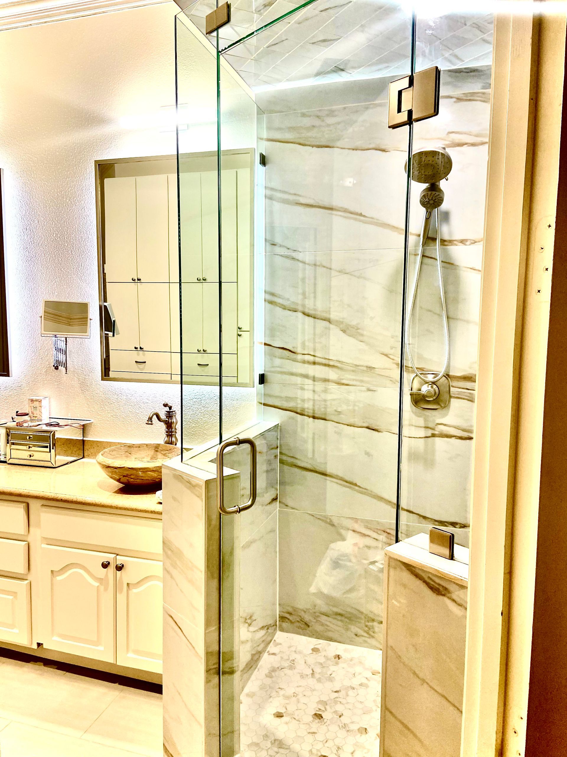Modern bathroom with glass shower enclosure, marble tile, and cream vanity in soft light