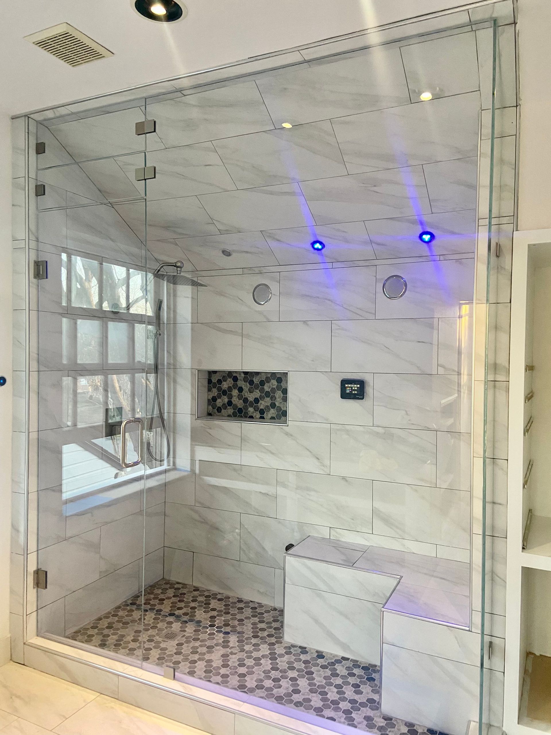 Modern glass shower enclosure with marble tile, mosaic floor, and blue LED ceiling lights