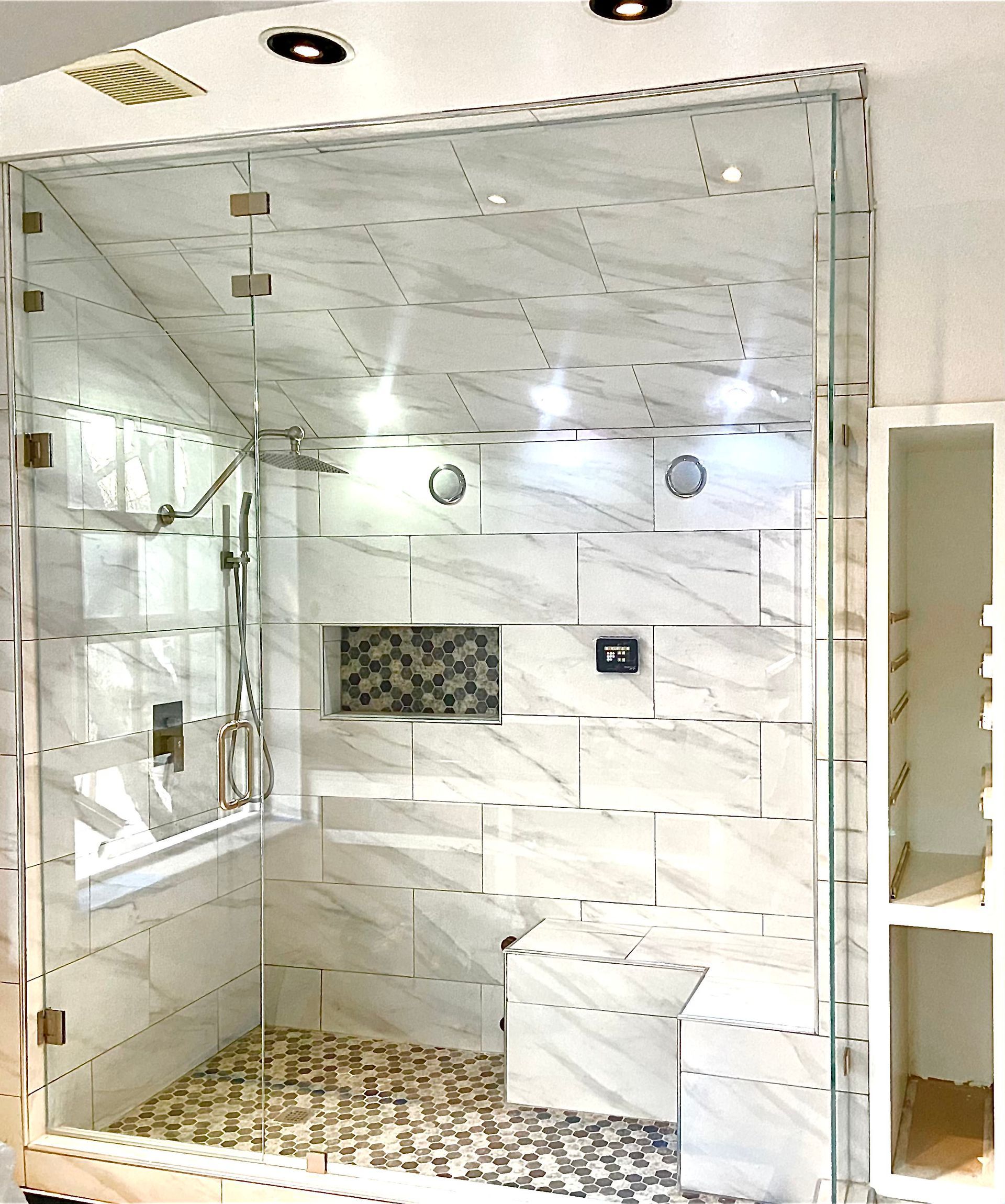 Modern tiled bathroom with glass shower enclosure, marble-look walls, mosaic floor, and built-in shelf