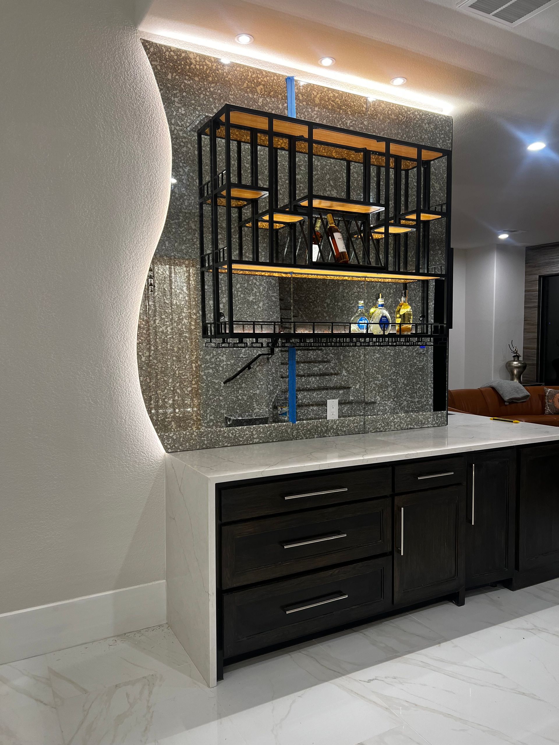 Modern kitchen wall with black cabinets, white countertop, and a lit mirrored shelf display.