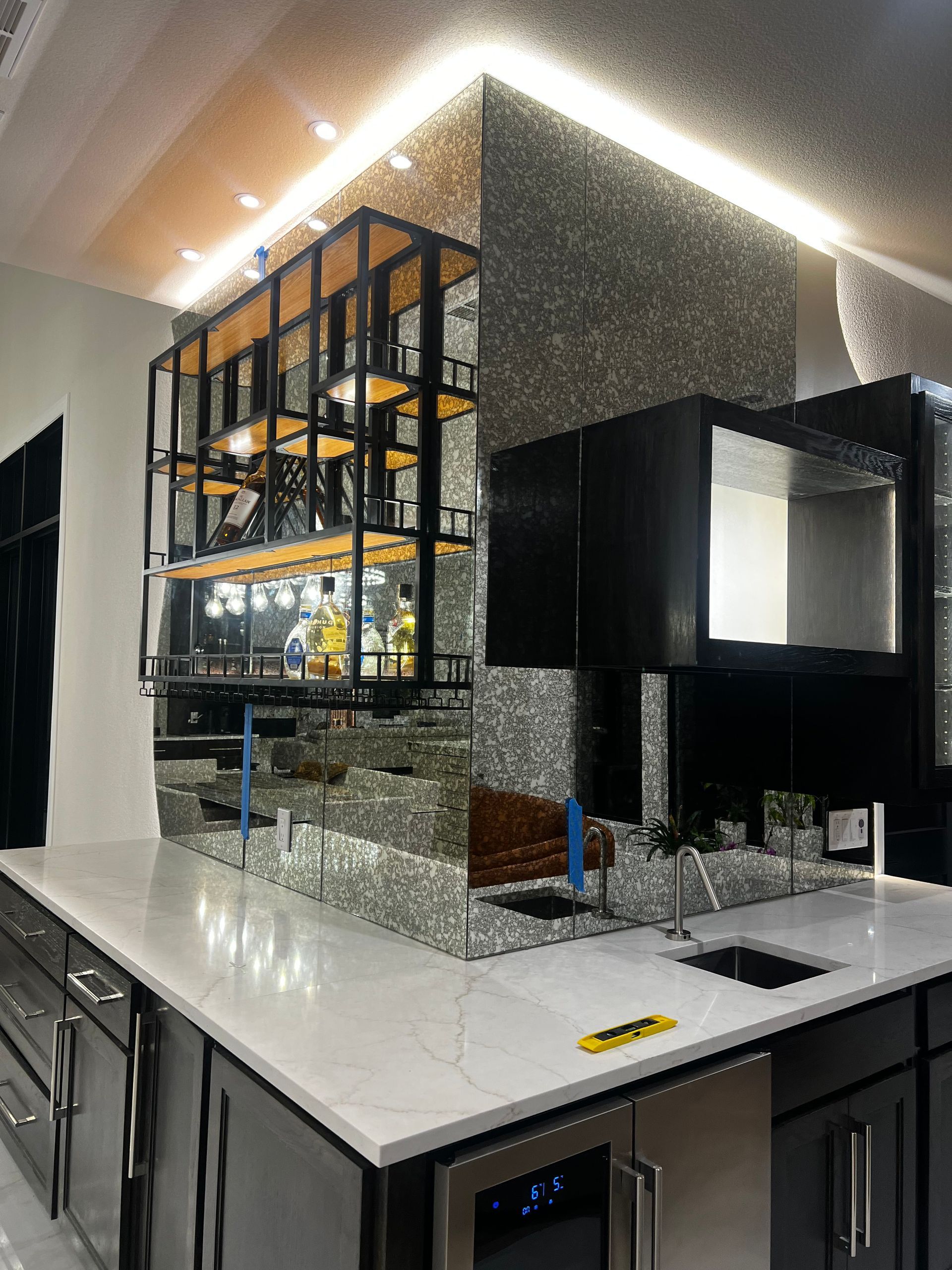 Modern kitchen with glossy black cabinets, white countertop, mirrored backsplash, and a metal shelf display