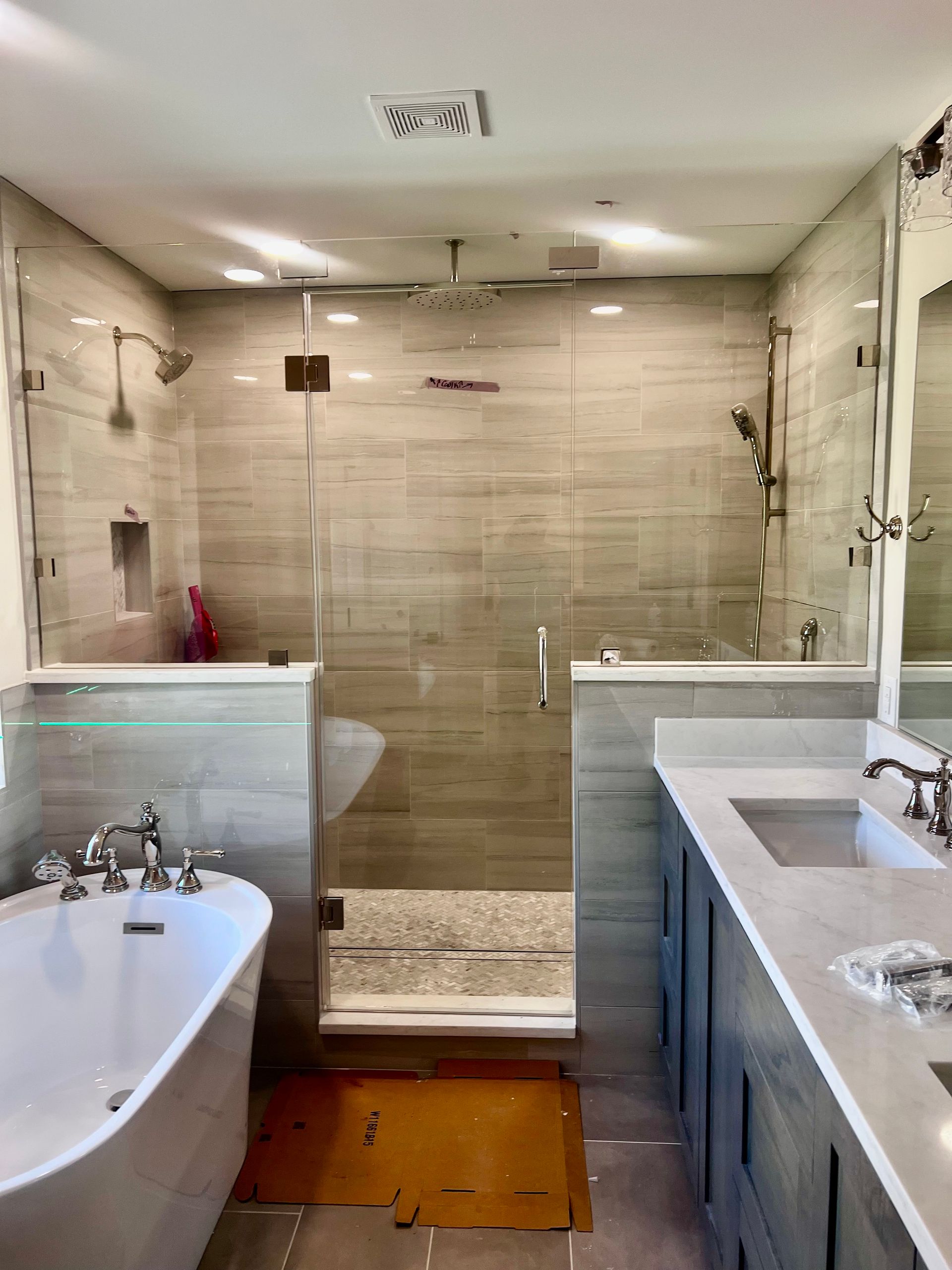 Modern bathroom with a glass walk-in shower, bathtub, and double sink vanity, seen from the doorway