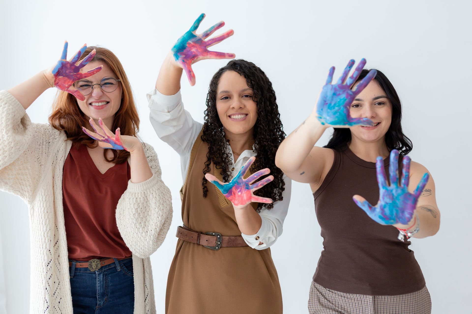 Três mulheres estão posando para uma foto com as mãos pintadas em cores diferentes.