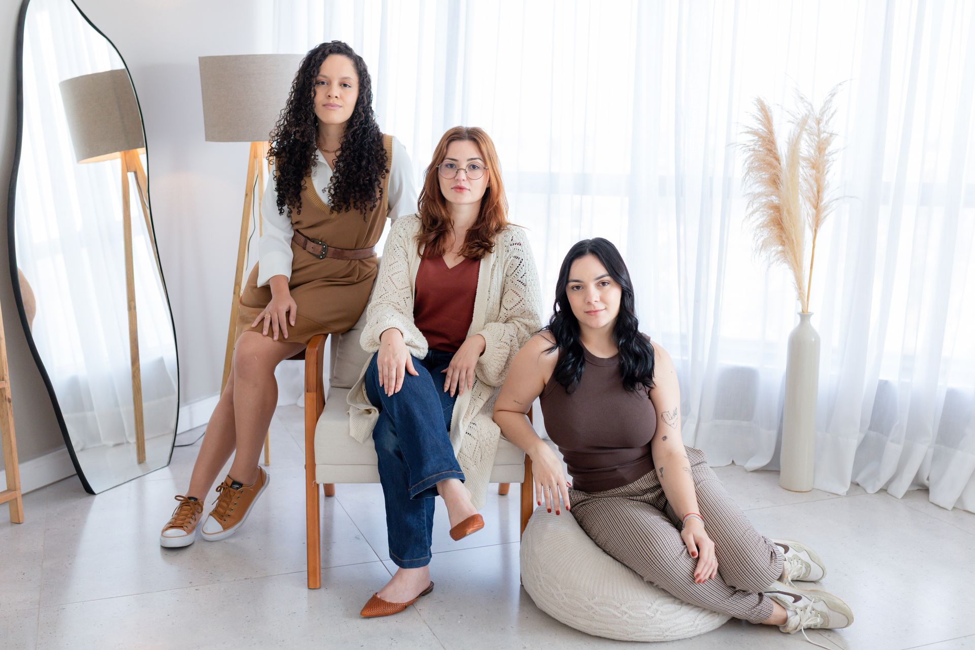 Três mulheres estão posando para uma foto sentadas em cadeiras e sentadas no chão.