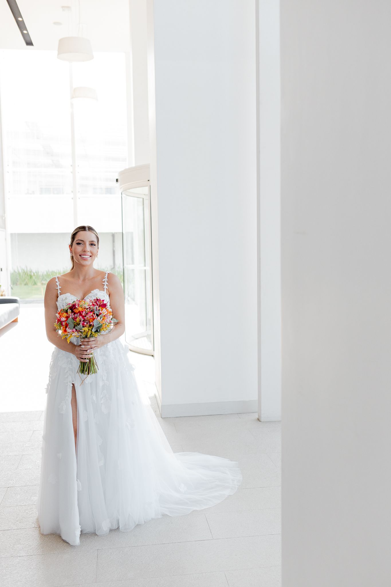 Noiva em um vestido de noiva branco com um buquê de flores, em pé em um edifício moderno e iluminado, com grandes janelas e colunas.