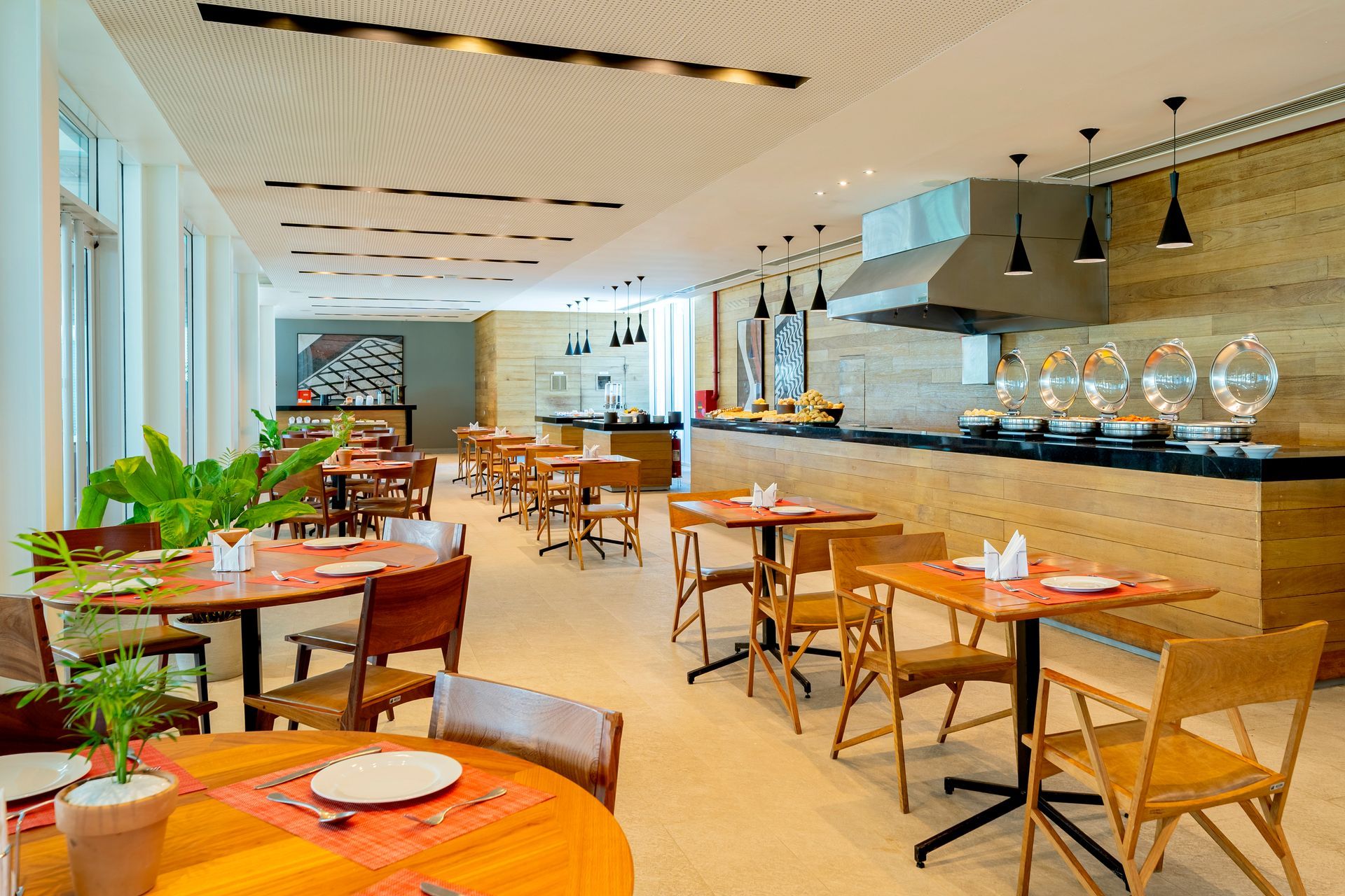 Um restaurante com interior iluminado, mesas e cadeiras de madeira, um bufê e um grande exaustor de cozinha.