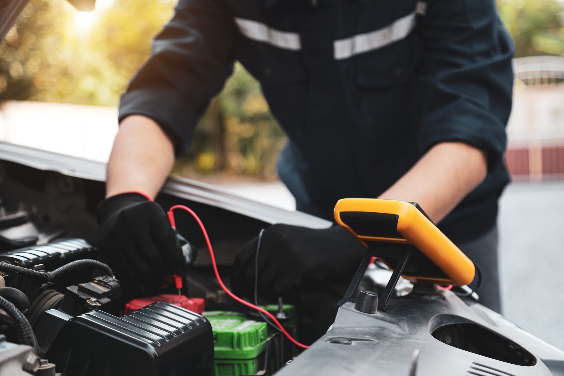Mechanic checking car engine with red and black jumper cables in an open hood