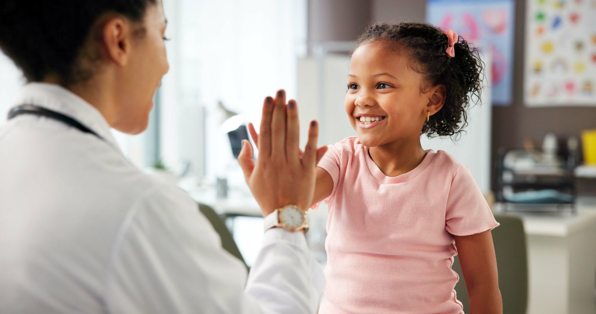 Doctor and young patient exchanging a high five during a medical visit in an exam room.