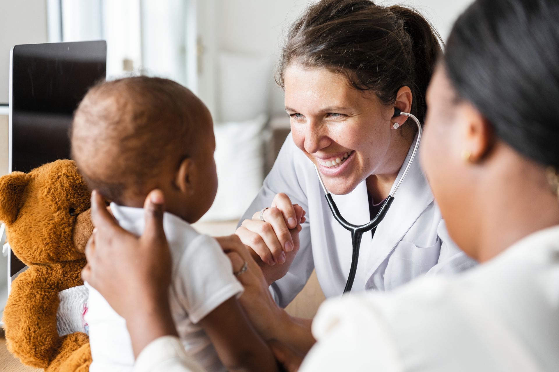 Clinician using a stethoscope to examine an infant held by a caregiver during a pediatric checkup. Clinician using a stethoscope to examine an infant held by a caregiver during a pediatric checkup.