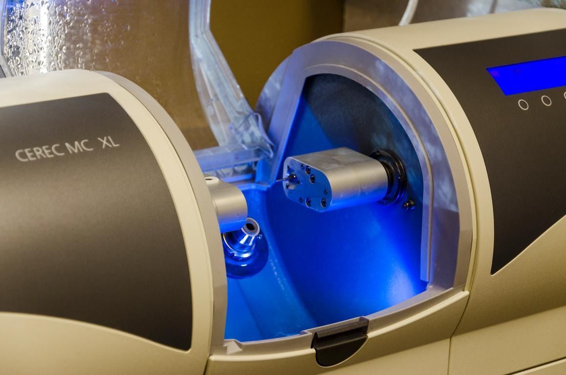 Dental milling machine, CEREC MC XL, milling a tooth restoration. Blue light illuminates the interior.