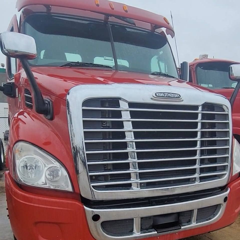 Front view of a red Freightliner semi-truck with a shiny chrome grille and bumper parked outdoors.