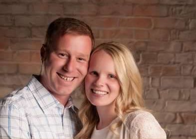 A man and a woman are posing for a picture in front of a brick wall.
