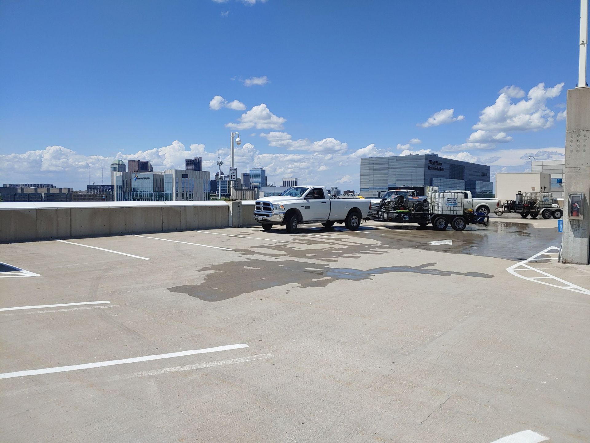 Two white trucks are parked in a parking lot with a city in the background