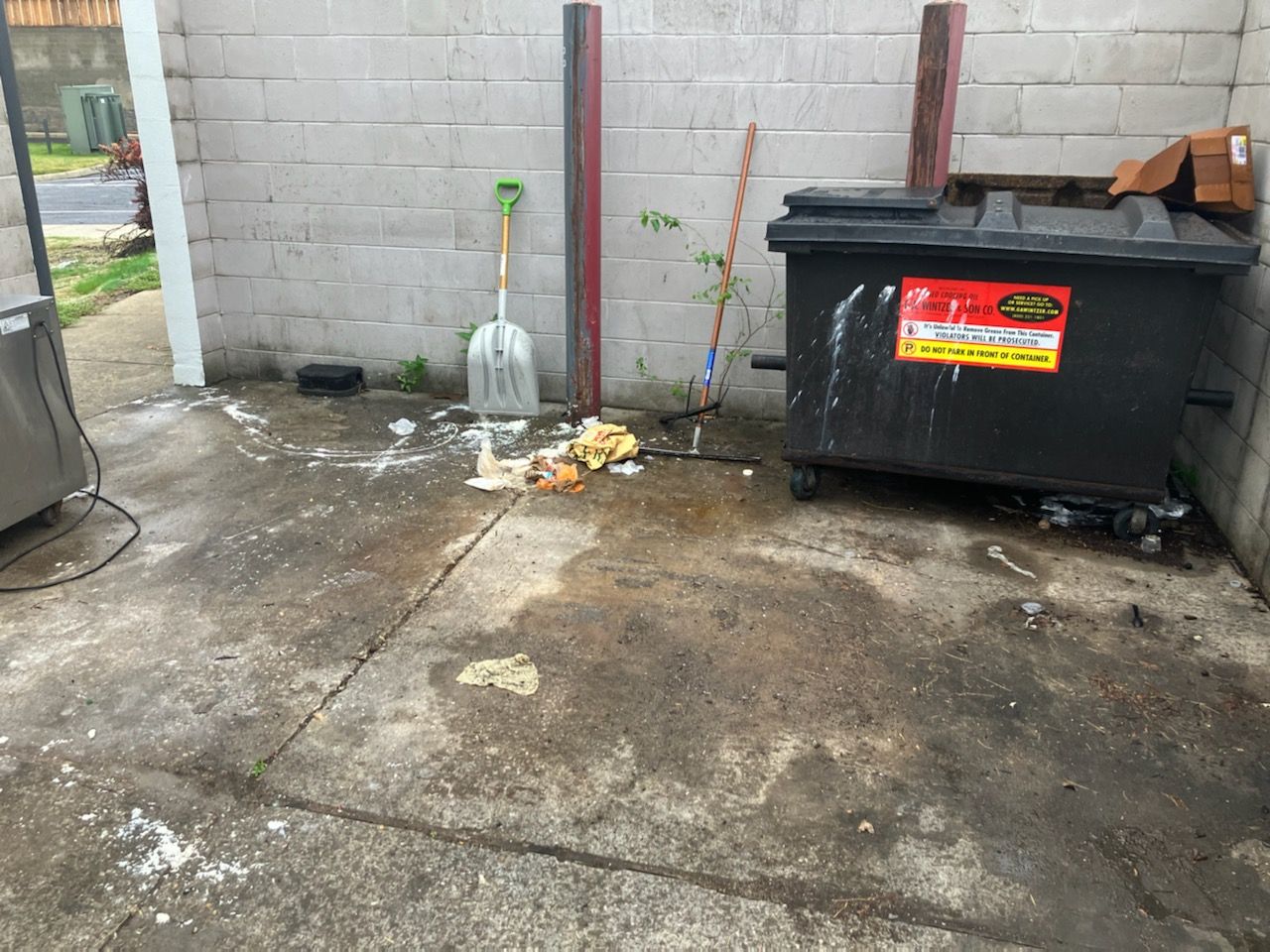 A trash can is sitting on the sidewalk next to a brick wall.