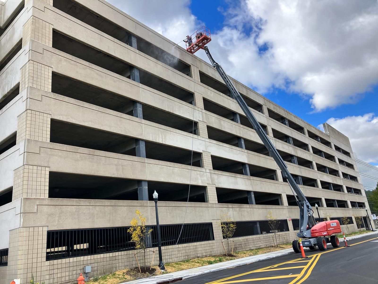 A crane is cleaning the side of a parking garage.