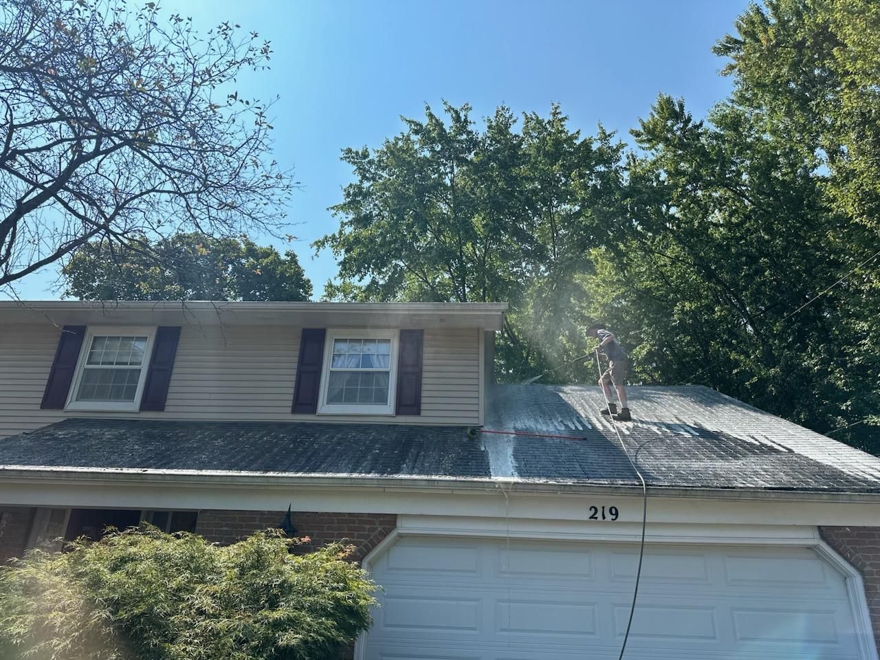 A man is cleaning the roof of a house with a pressure washer.