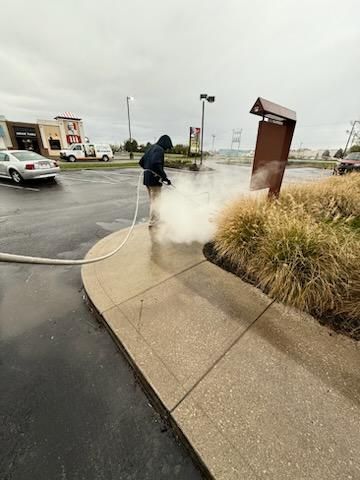 A man is cleaning a sidewalk with a hose.