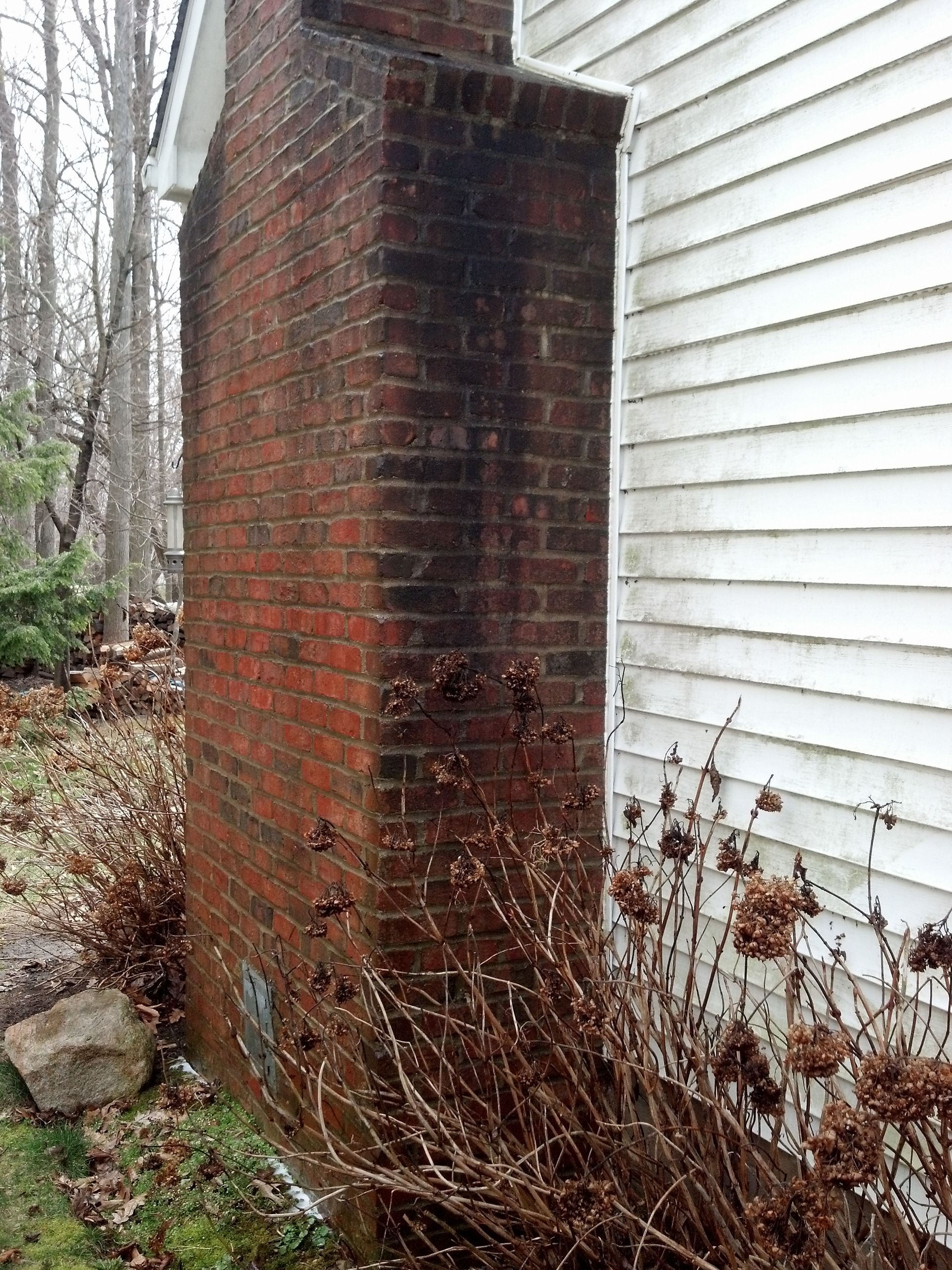 A brick chimney is sitting next to a white house before soft wash clean.