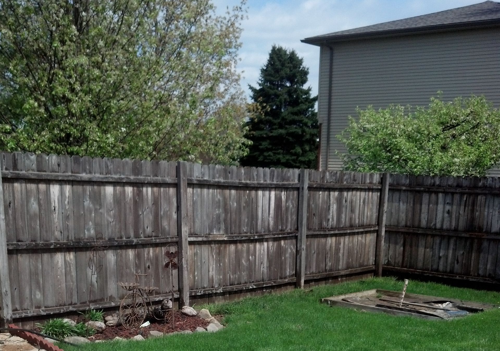 A backyard with a wooden fence and a house in the background