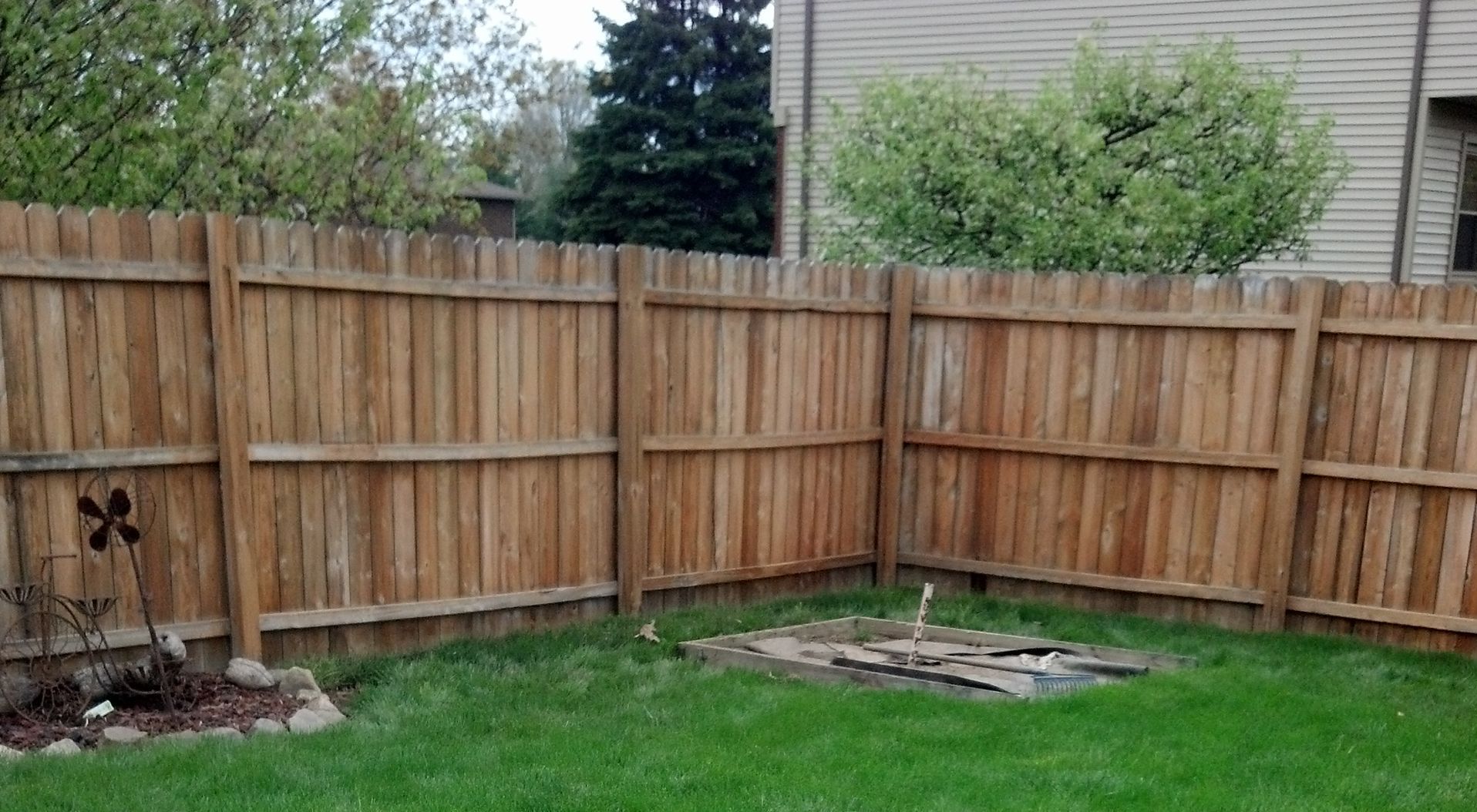 A wooden fence surrounds a lush green lawn in a backyard.