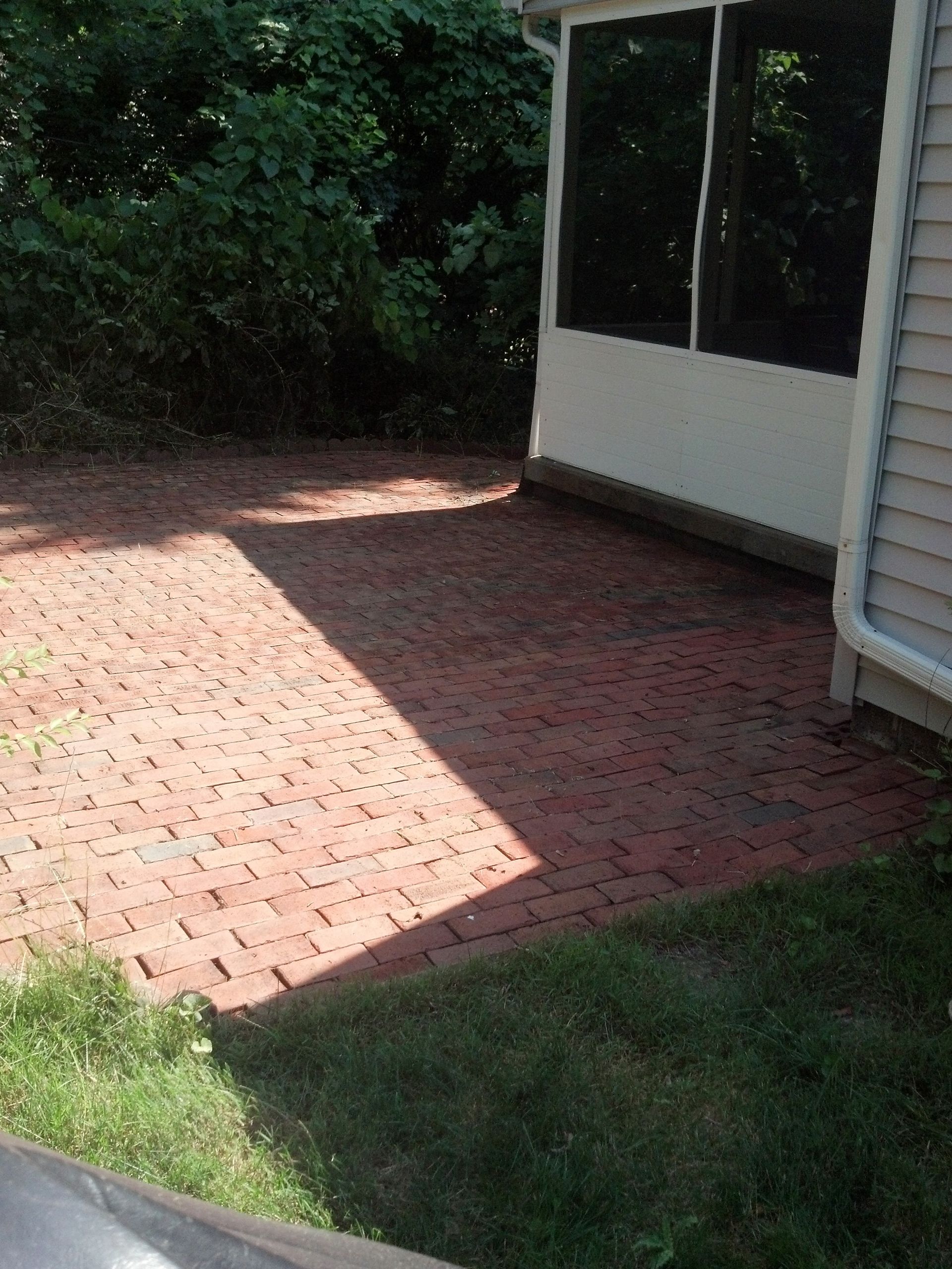 A brick patio in front of a house with a screened in porch