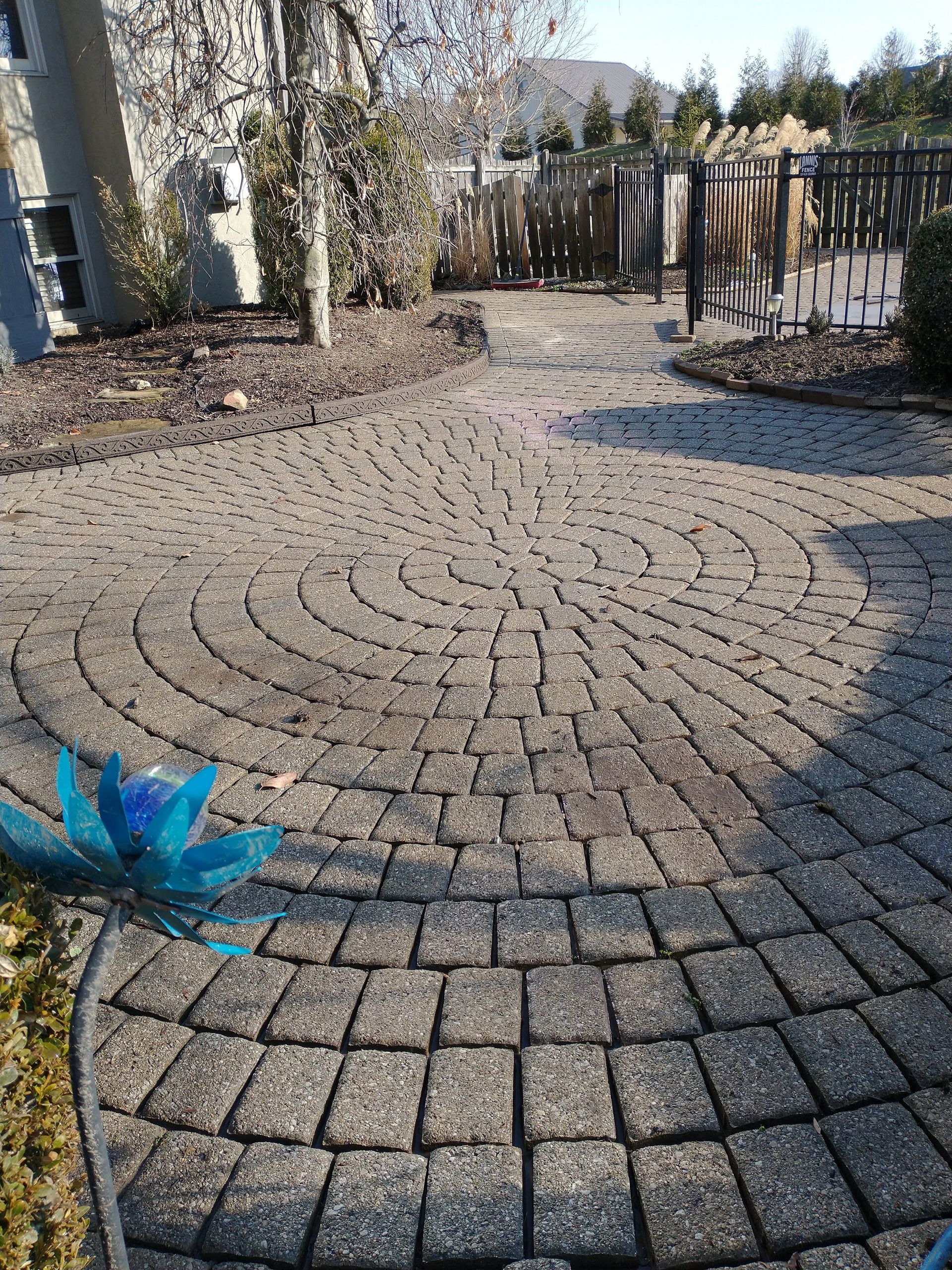 A brick walkway leading to a house with a blue flower in the middle.