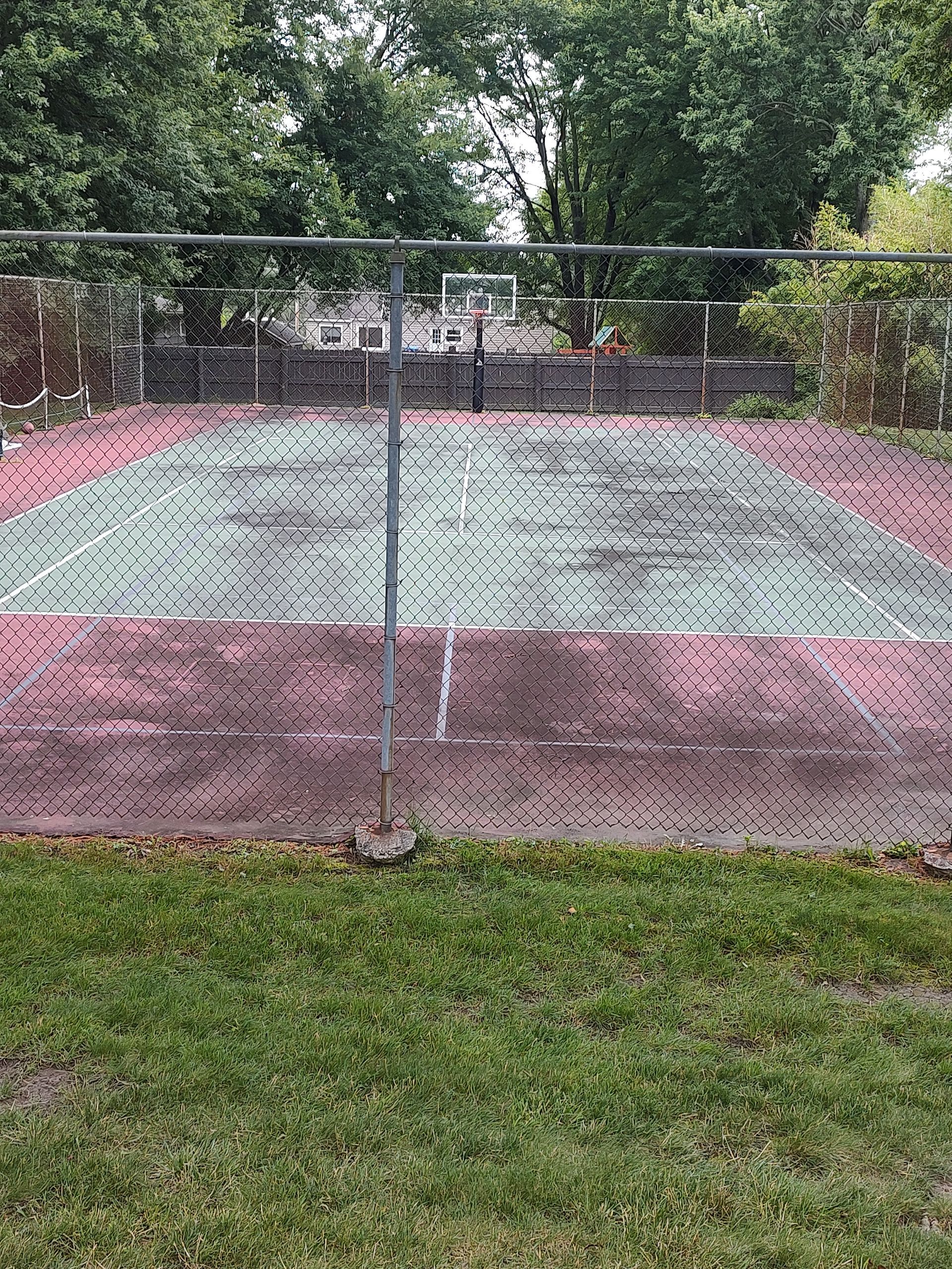 A basketball court behind a chain link fence in a park.