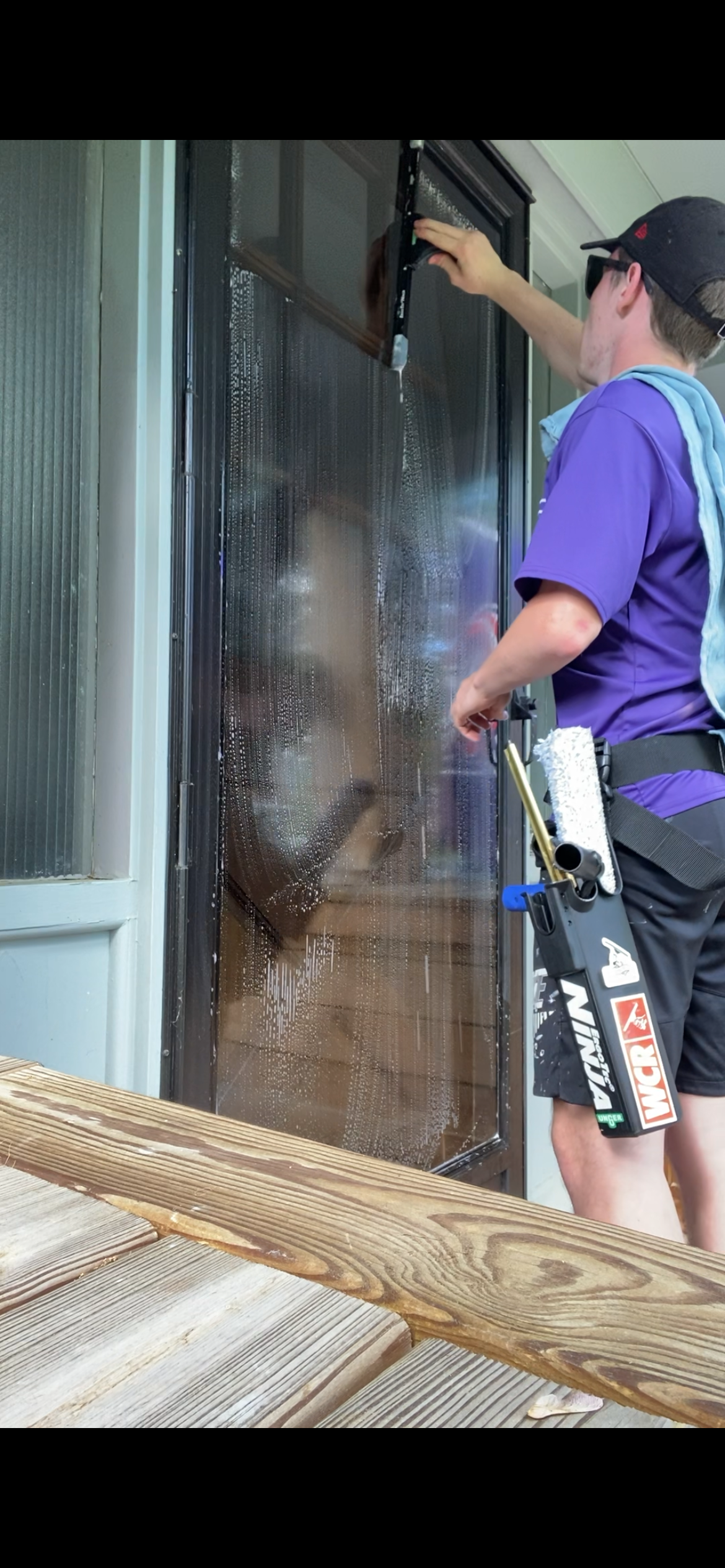 A man in a purple shirt is cleaning a window.