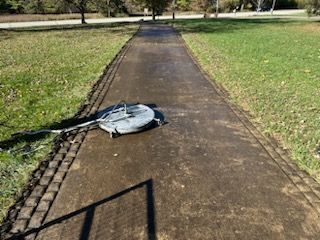 A lawn mower is sitting on the side of a path in a park.