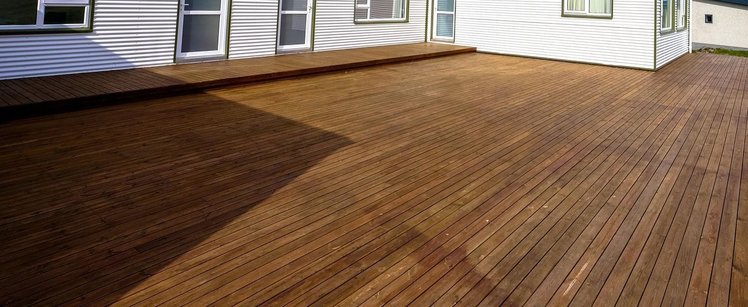 A large wooden deck with a white house in the background