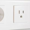 Close-up of a white electrical outlet with a standard NEMA 5-15 receptacle next to a partially visible circular outlet.
