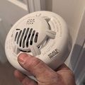A hand holding a white smoke detector that has a label reading