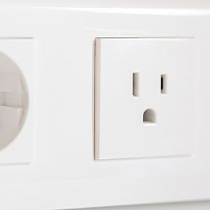 Close-up of a white electrical outlet with a standard NEMA 5-15 receptacle next to a partially visible circular outlet.