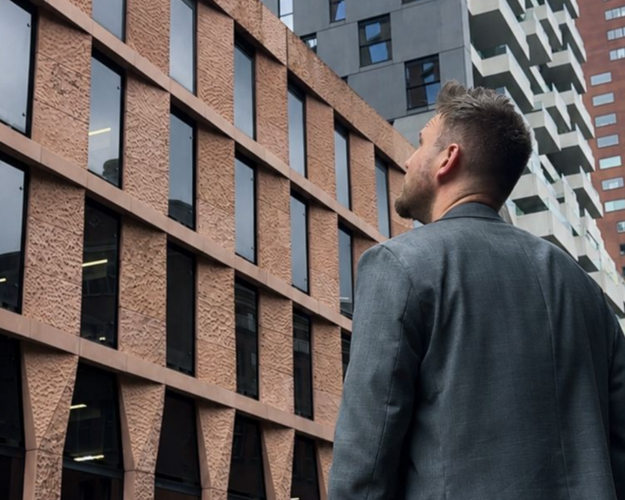 Man in a gray coat looking up at modern brick and glass office buildings