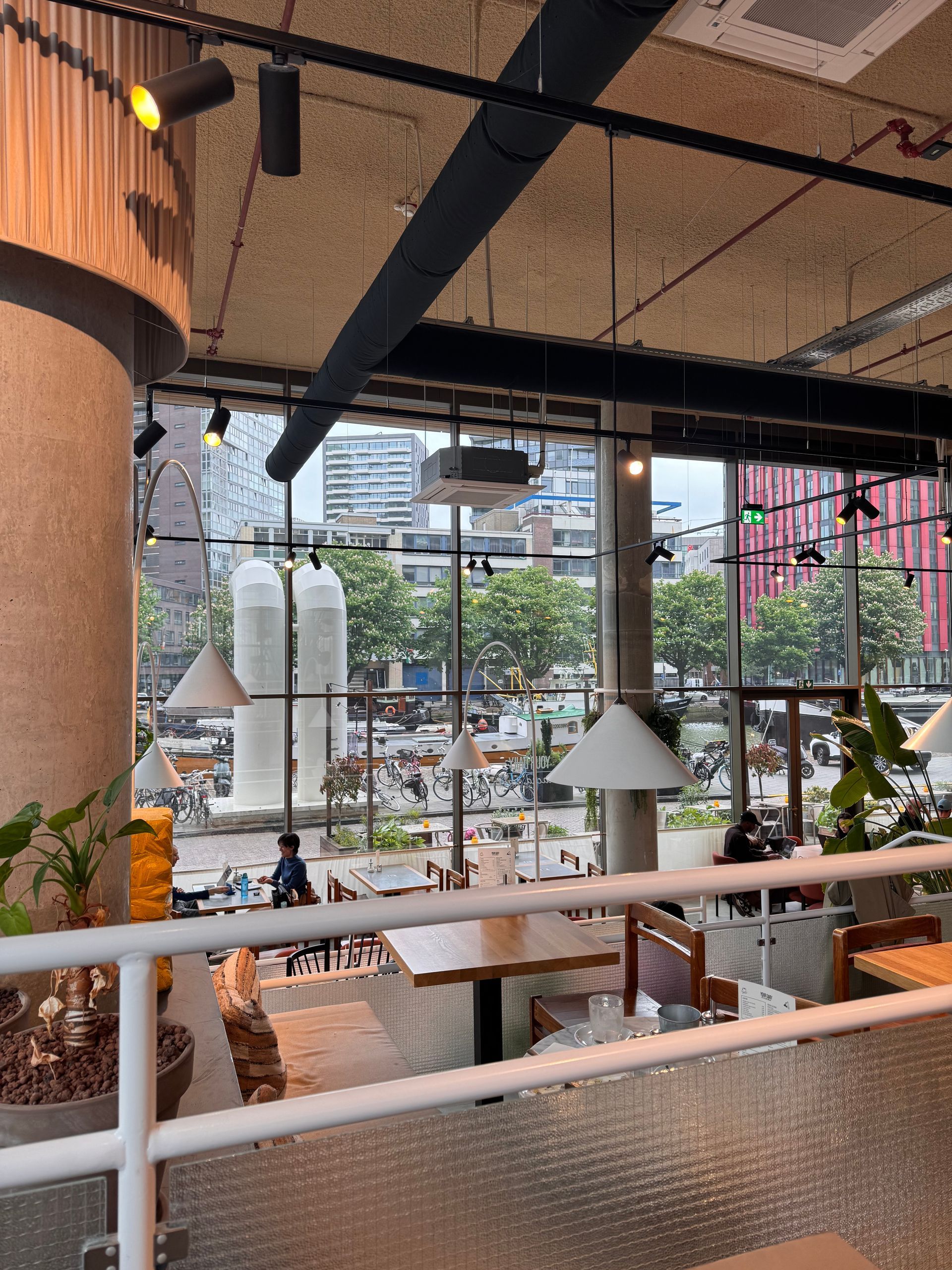 Bright café interior with hanging pendant lights, plants, and large windows overlooking city buildings